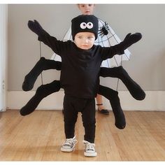 a young boy is standing in front of a giant spider costume with two smaller boys behind him