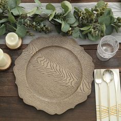 a place setting with plates, silverware and greenery on a wooden table top