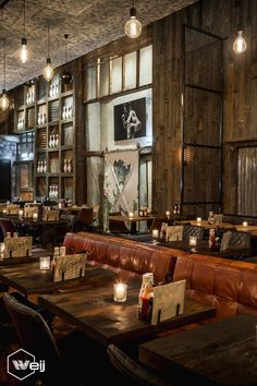 a restaurant with wooden tables and leather couches, lit by candlelight bulbs hanging from the ceiling