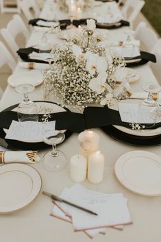 the table is set with black and white plates, silverware, flowers, and candles