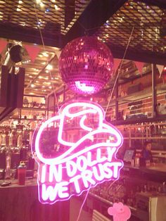 a neon sign that says in doly we trust hanging from the ceiling above a disco ball