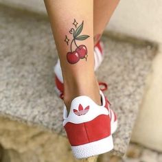 a woman's foot with a cherry tattoo on her left leg and red tennis shoes