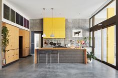 a kitchen with yellow cabinets and gray flooring next to a bar area that has two stools on it