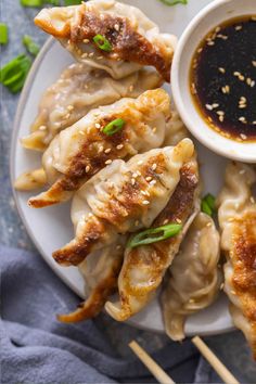 some dumplings on a plate with dipping sauce and chopsticks next to them