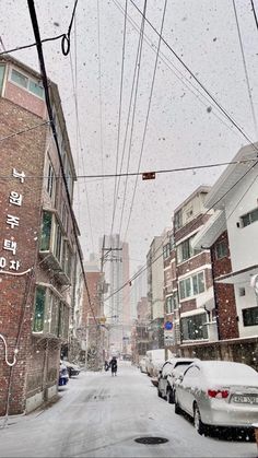 cars parked on the side of a snow covered street next to tall buildings and power lines