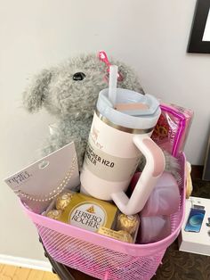 a teddy bear sitting on top of a pink basket filled with food and drink items