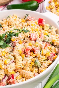 a white bowl filled with pasta salad next to green onions and red bell pepper peppers