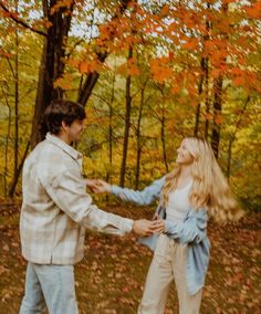 a man and woman are dancing in the woods with autumn leaves on the ground behind them