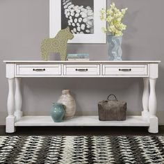 a white console table with two drawers and vases on the top, in front of a gray wall