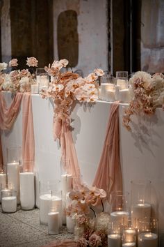 a table with candles and flowers on it in front of a wall filled with white vases