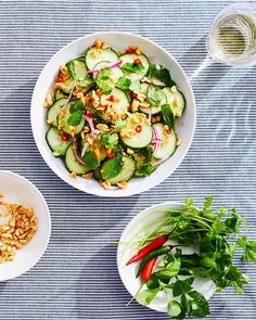 two white bowls filled with cucumbers, onions and other vegetables on top of a blue table cloth