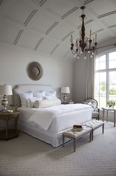 a bedroom with a large bed, chandelier and two tables in front of the window