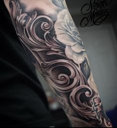 a man's arm with flowers and swirls in black and grey ink on it