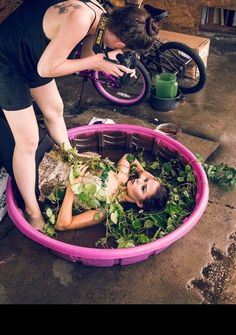 a woman in a pink tub with plants on the ground next to a man and bicycle