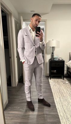 a man in a suit taking a selfie with his cell phone while standing in a living room