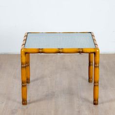 a small table made out of bamboo sticks and glass topped with blue top sitting on a wooden floor