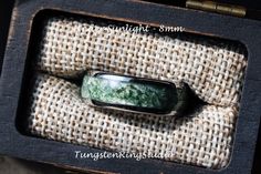 a ring with green and black marble in it sitting inside a wooden box on top of burlied fabric