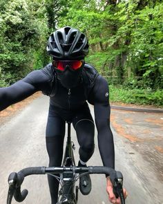 a man riding a bike down a road next to lush green trees