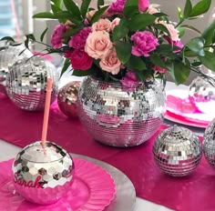 a table topped with pink plates and silver vases filled with flowers next to disco balls