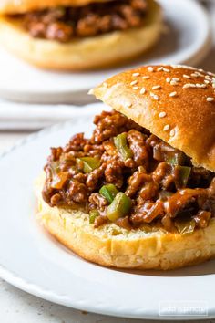 a sloppy joe sandwich on a plate with another sandwich in the back ground behind it