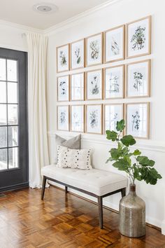 a living room with pictures on the wall and a bench next to a plant in a vase