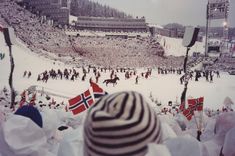 a crowd of people standing on top of a snow covered field next to a ski slope