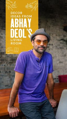 a man sitting on top of a wooden table next to a yellow sign that says decor ideas from abhay deol's own room