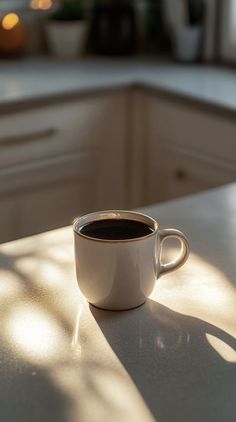 a cup of coffee sitting on top of a white counter next to a window in a kitchen