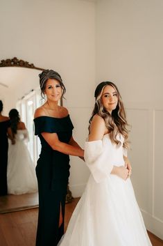 two women standing next to each other in front of a mirror wearing black and white dresses