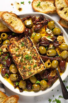 a white plate topped with olives and fish next to slices of toasted bread