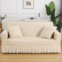 a white couch sitting on top of a hard wood floor next to a green plant