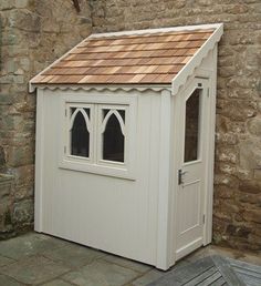 a small white shed sitting next to a stone wall with a wooden table and chairs