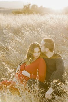 a couple cuddles in tall grass during their engagement photo session at the park