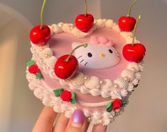 a hello kitty cake with cherries and cherries on top is being held up