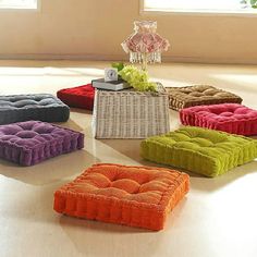 four different colored cushions sitting on top of a white floor next to a vase with flowers