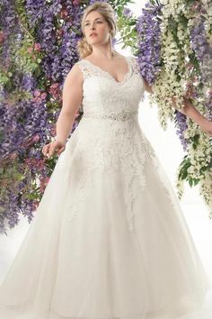 a woman in a wedding dress standing next to purple and white lilac flowers, with her hands on her hips