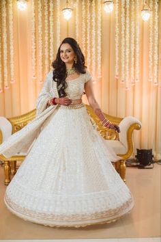 a woman in a white dress standing next to a gold chair and curtained wall