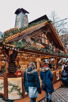 two people standing in front of a food stand with christmas decorations on the roof and windows