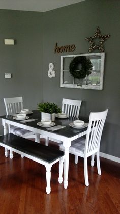 a dining room table with white chairs and plates on top of it, in front of a gray wall