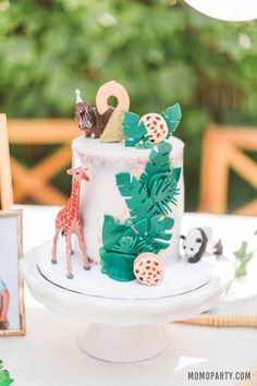 a white cake with green leaves and animals on it sitting on top of a table