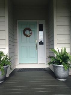 two planters are on the front porch with a blue door and green wreath above it