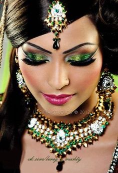 a woman with green and gold makeup looks down at her face while wearing an elaborate headpiece