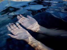 two hands reaching out to the water with their reflection on it's surface,