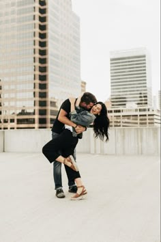 a man and woman are dancing on the roof in front of tall buildings with skyscrapers behind them