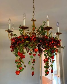 a chandelier hanging from the ceiling with red flowers and greenery on it