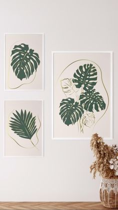 three green leaf prints hanging on the wall above a wooden table with a vase filled with flowers