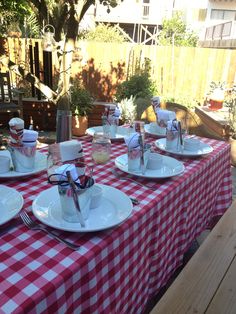 a red and white checkered table cloth with plates, cups and utensils on it