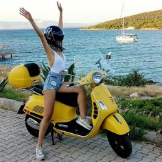 a woman riding on the back of a yellow scooter next to a body of water