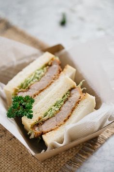 a sandwich with meat, lettuce and sauce in a paper container on a table