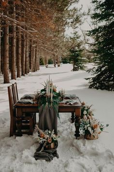 the table is set for dinner in the snow with flowers and greenery on it